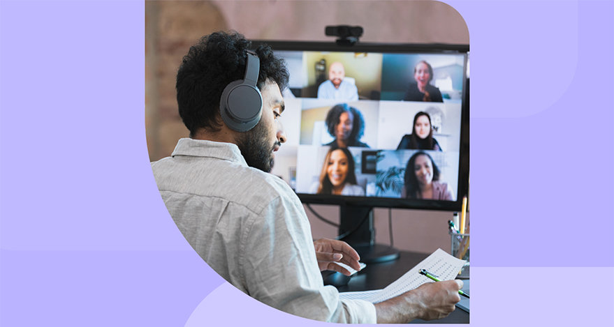 A man sits at his desk and is on a video conferencing call with several other people, whose faces appear on the computer screen.